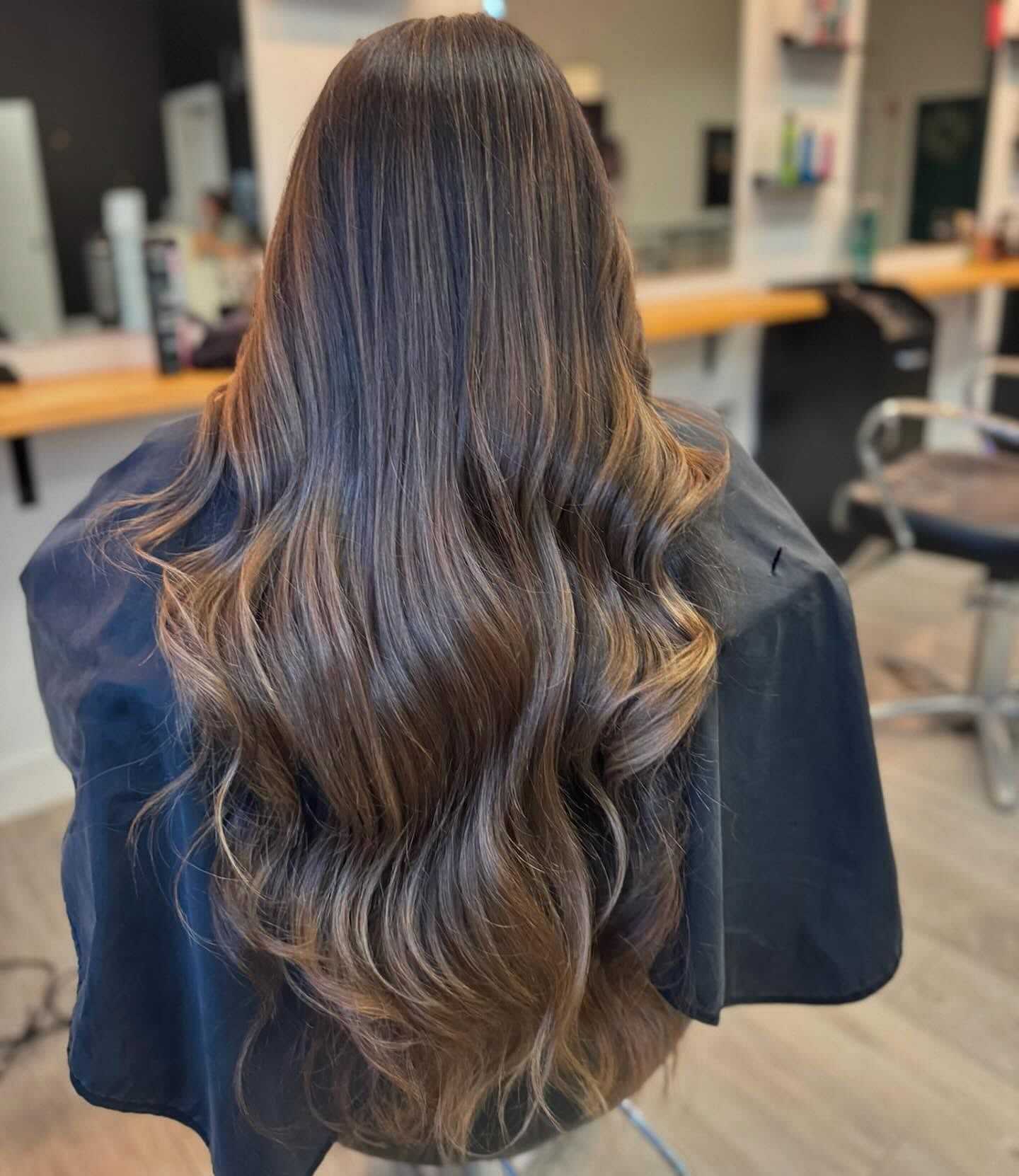 Woman with long, wavy, highlighted hair sitting in a salon chair, ready for a haircut.