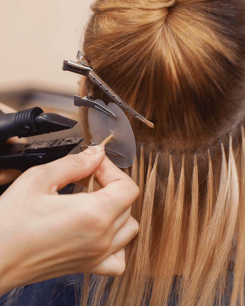 Hair extension being applied by a stylist, using tools to attach strands to natural hair.