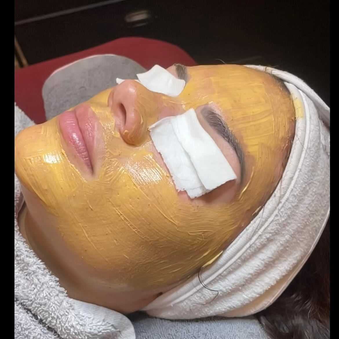 Woman relaxing with a facial mask and cotton pads on her eyes in a spa setting.